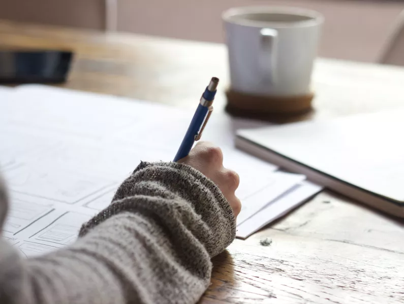 A hand in a grey long-sleeve sweater takes notes with a pen